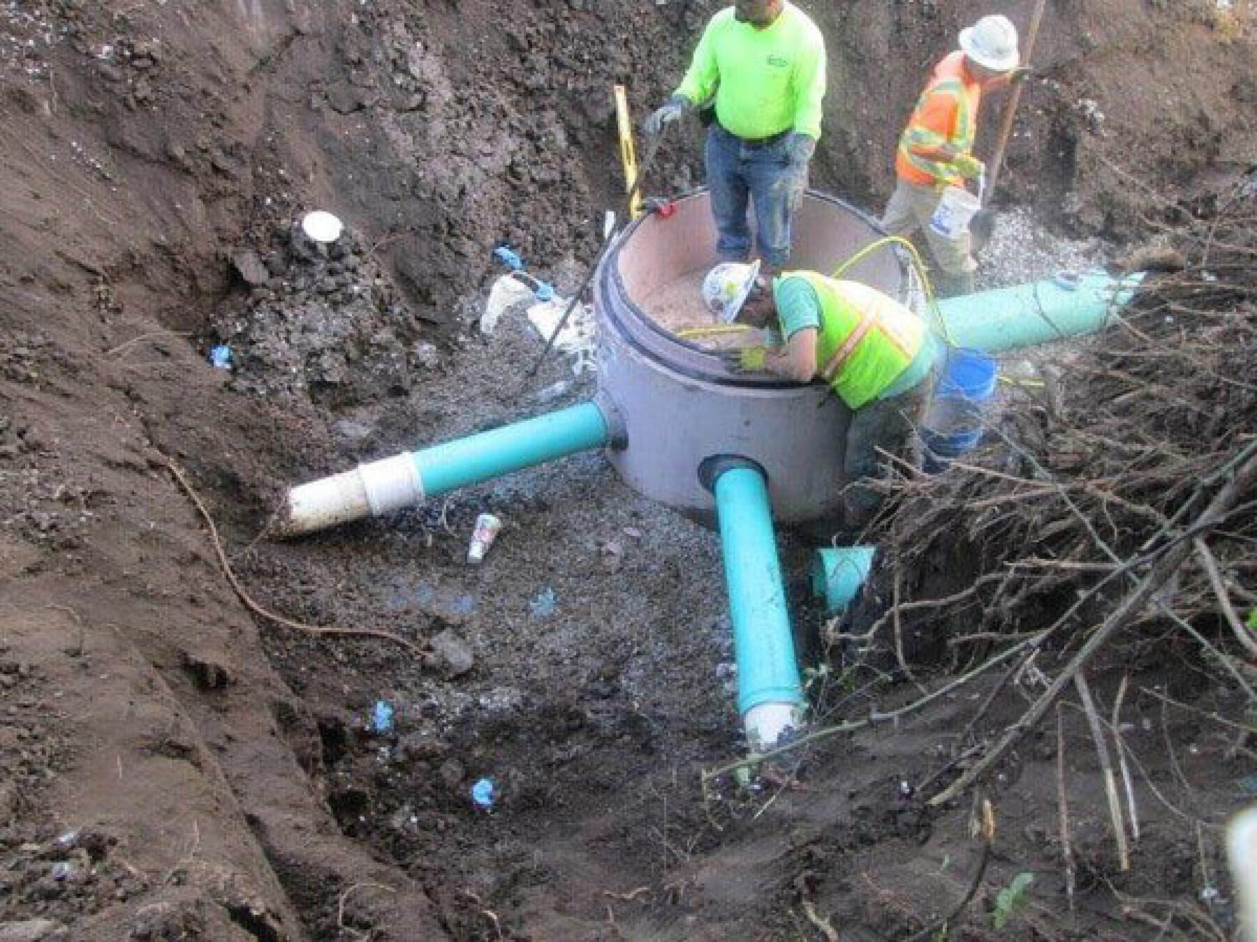Three workers install pipes in the ground.