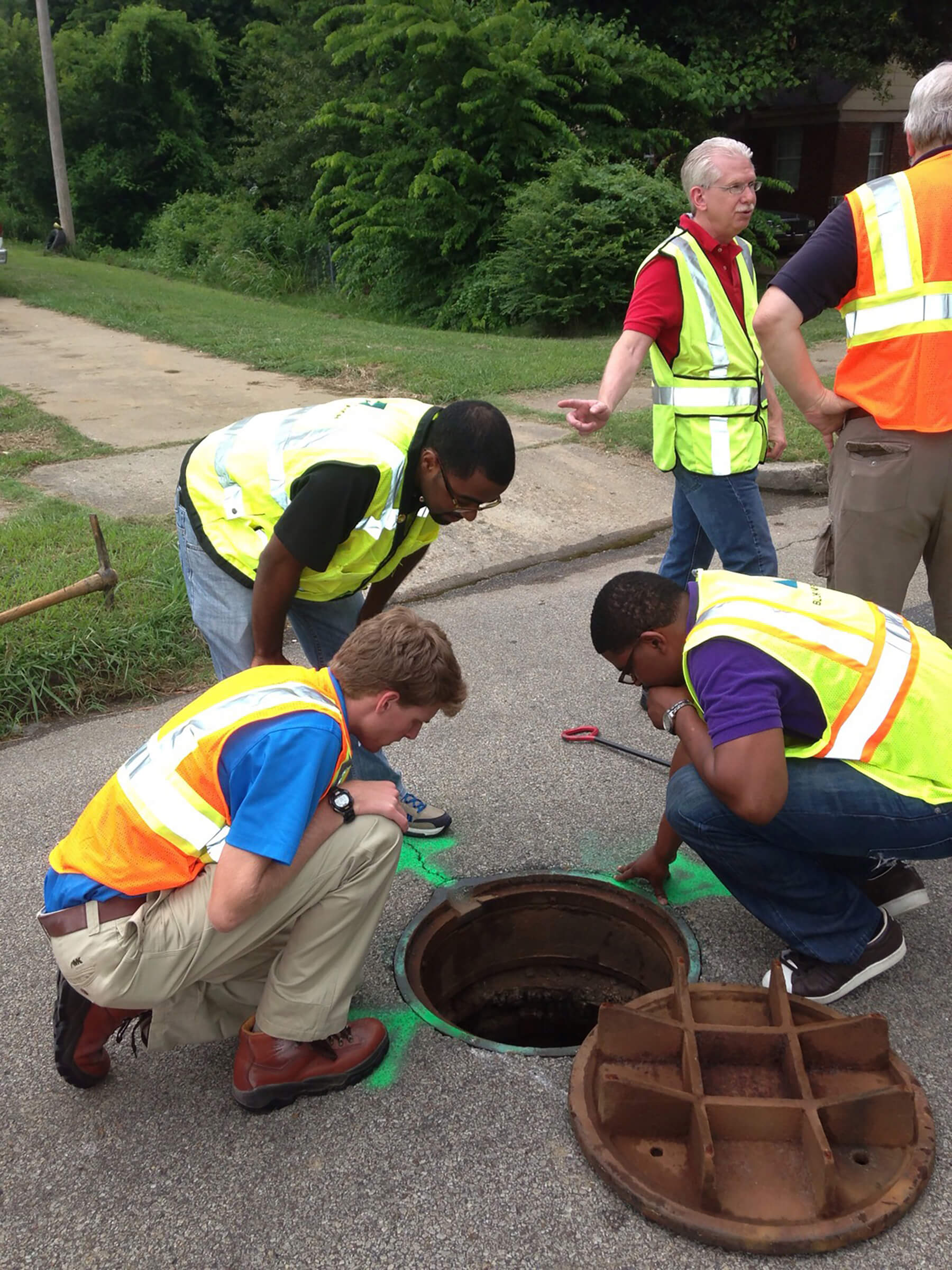 A group of workers in reflective vests looking down a manhole.