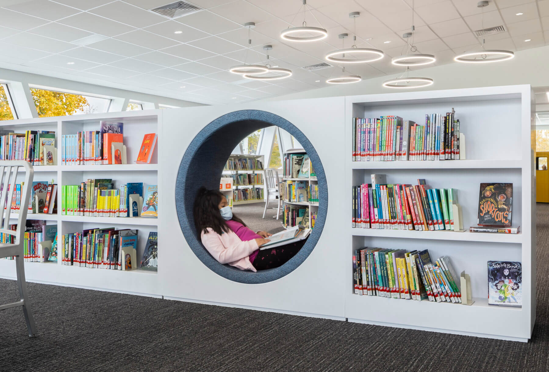 a young girl reads a book while sitting inside a circular nook built within the bookshelves