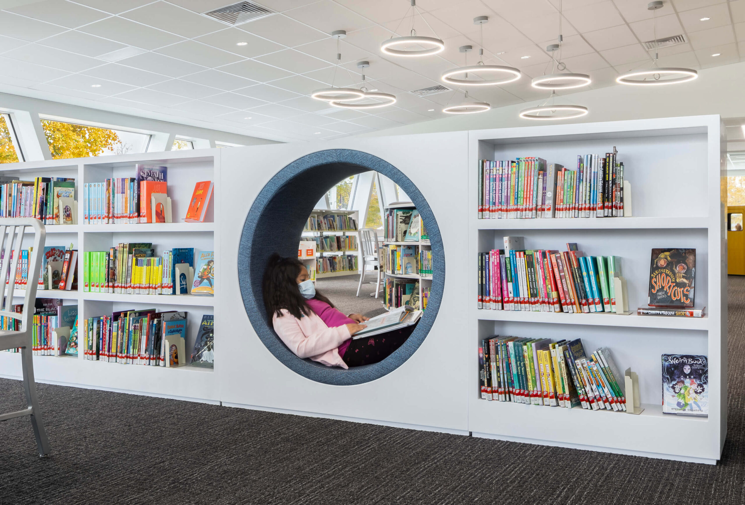 : a young girl reads a book while sitting inside a circular nook built within the bookshelves