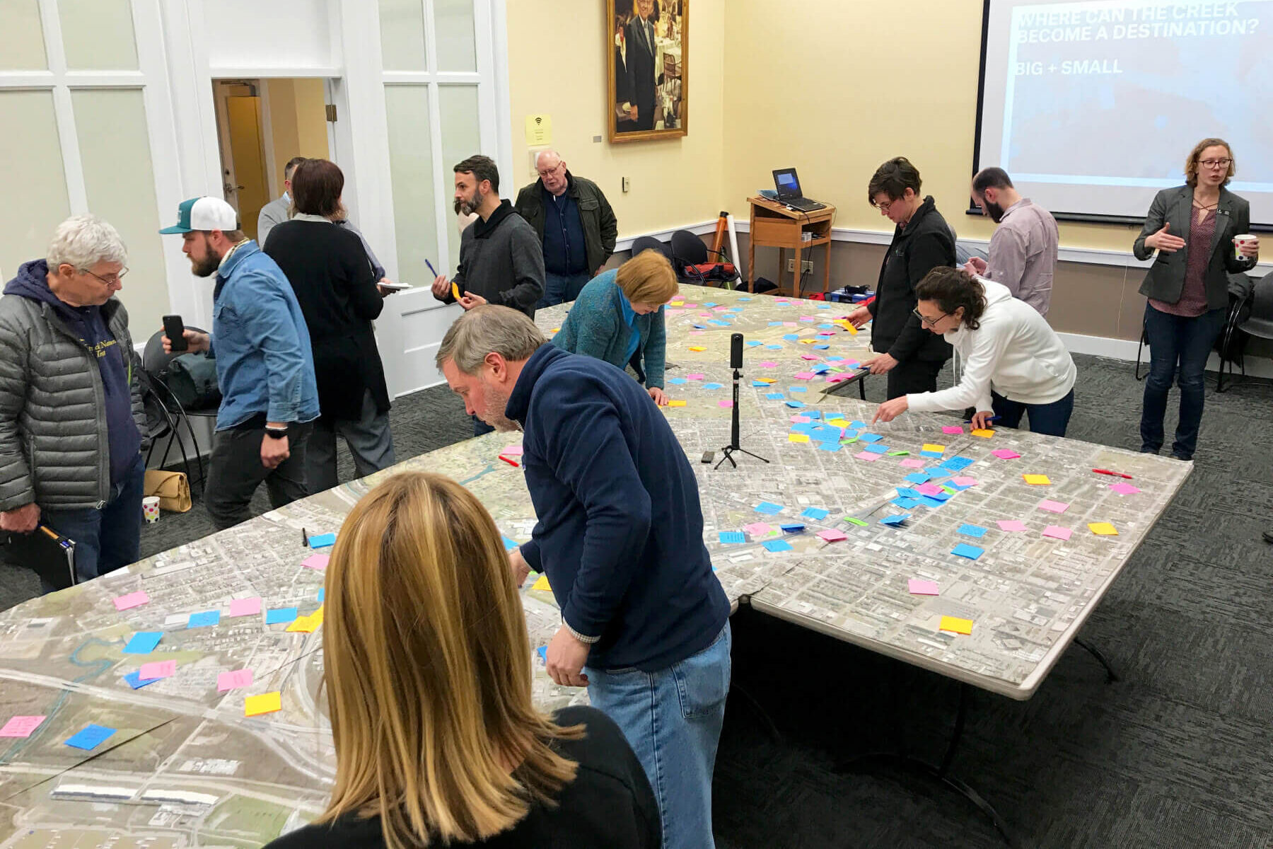 people gathered in a room around a large map laid out on tables