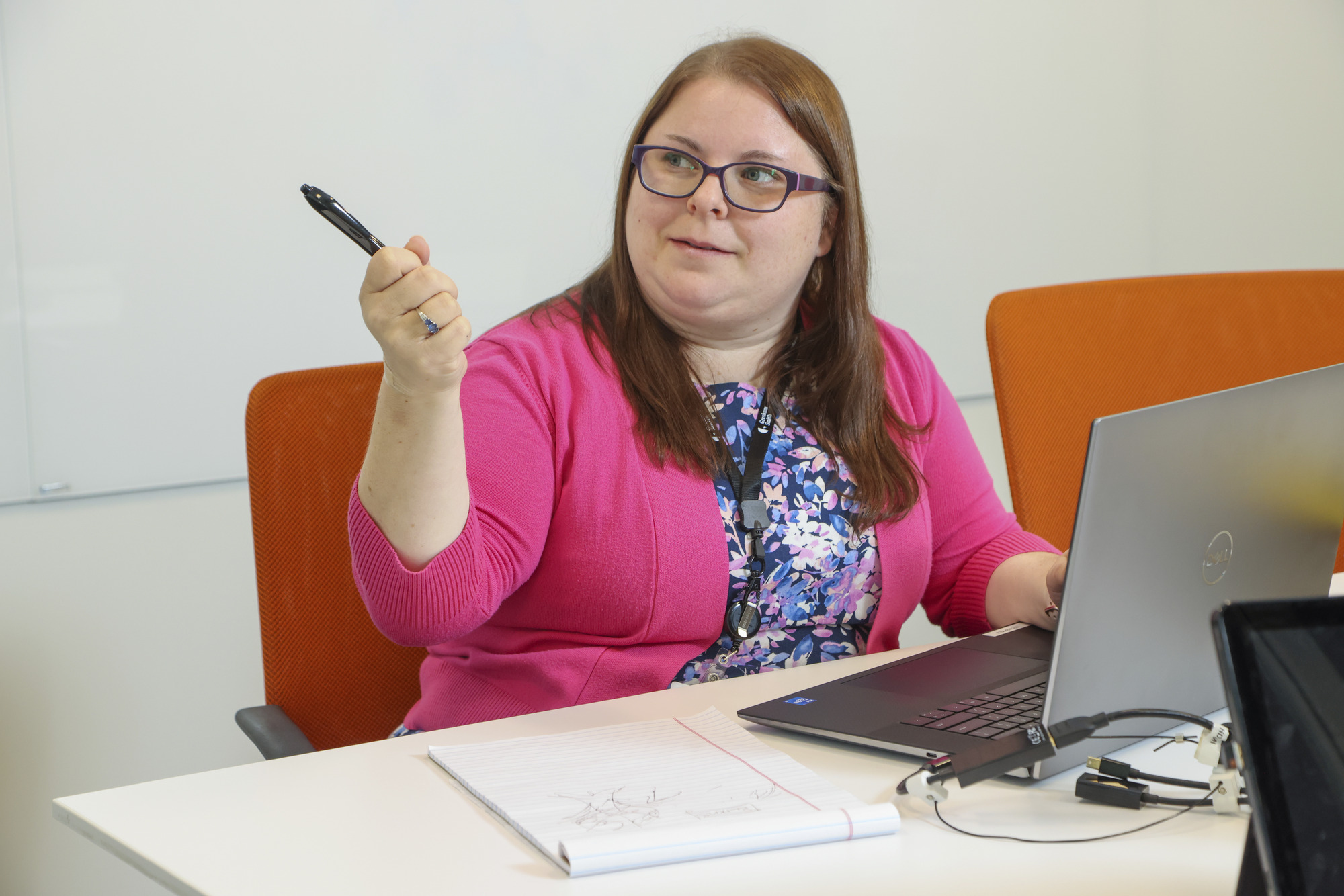 A person sitting at a table working on a laptop holding a pen and pointing at something