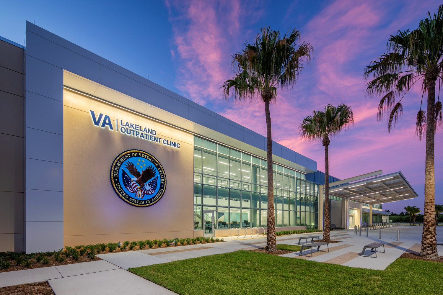 Exterior of a Veterans Affairs clinic with palm trees in front at dusk