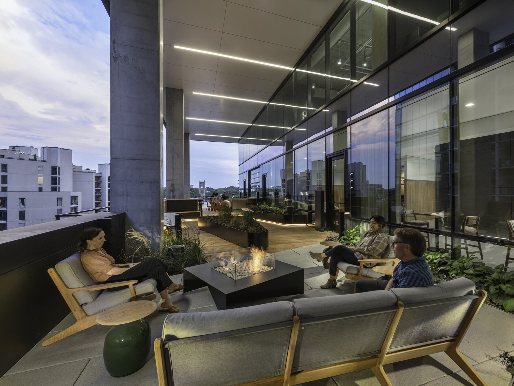 An outside terrace at sunset with three people sitting around a fire pit on outdoor soft seating.