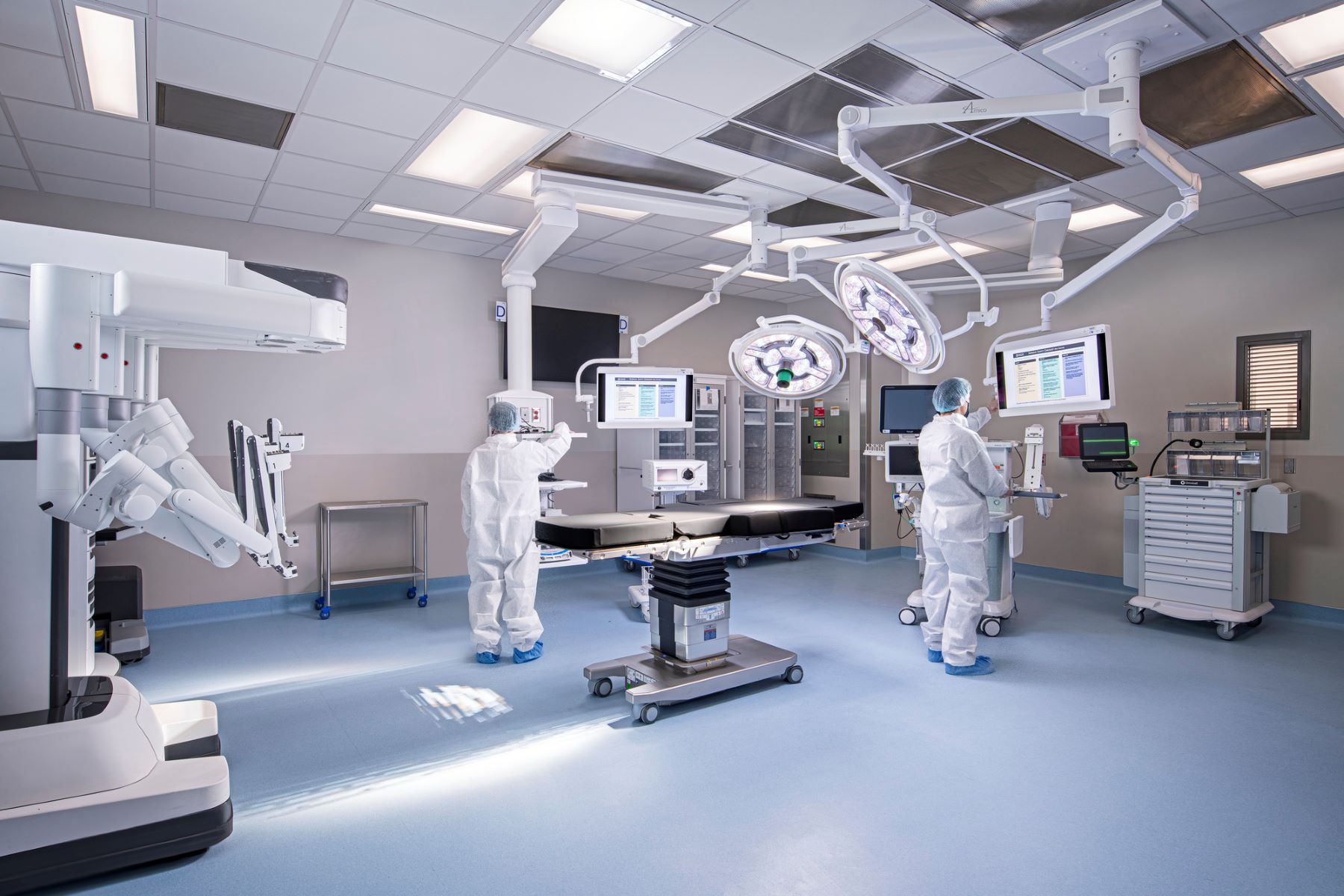 Two people in white paper scrubs standing at machines in an operating room