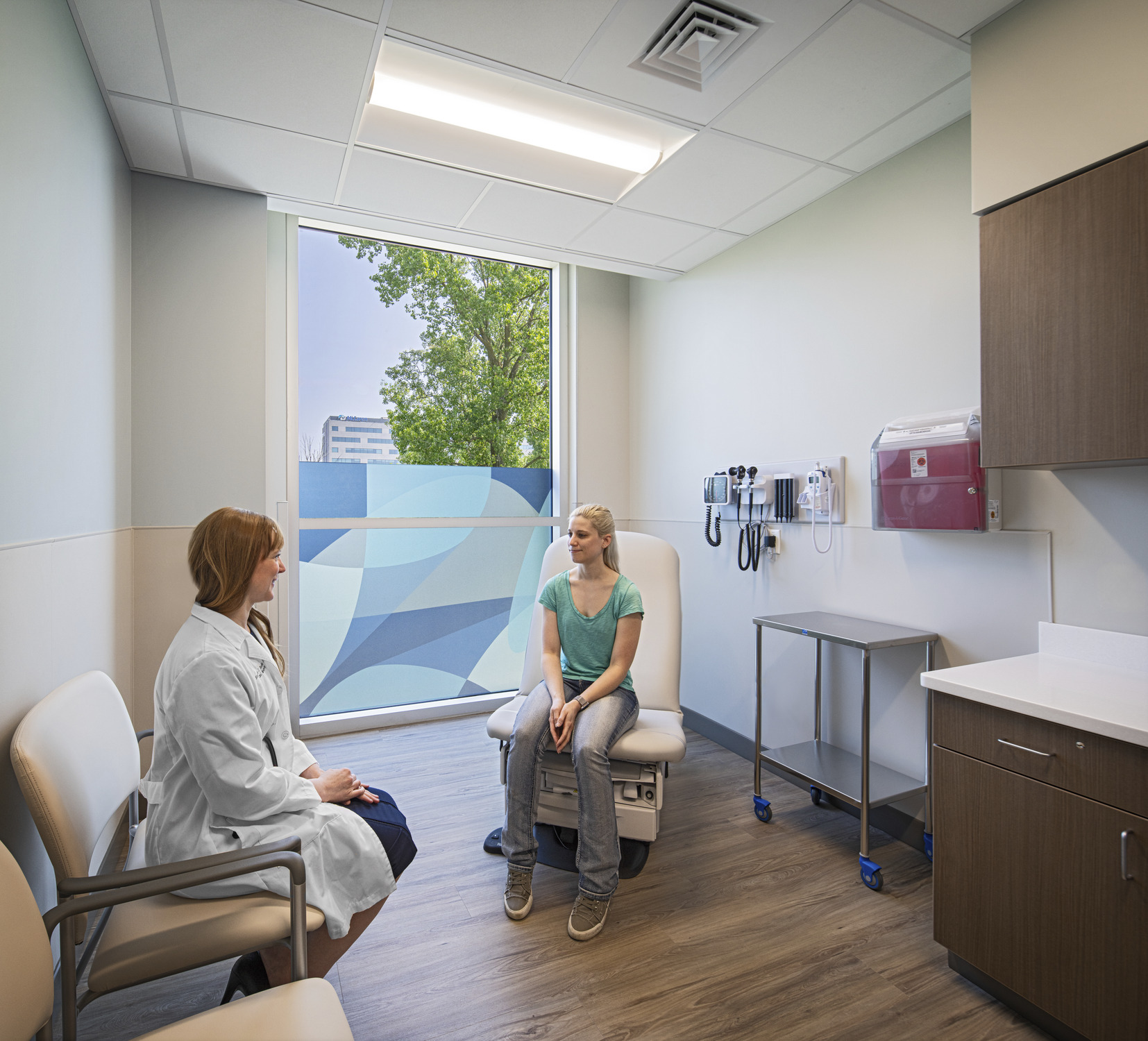 a doctor sitting on a chair next to a patient on an exam table in an exam room