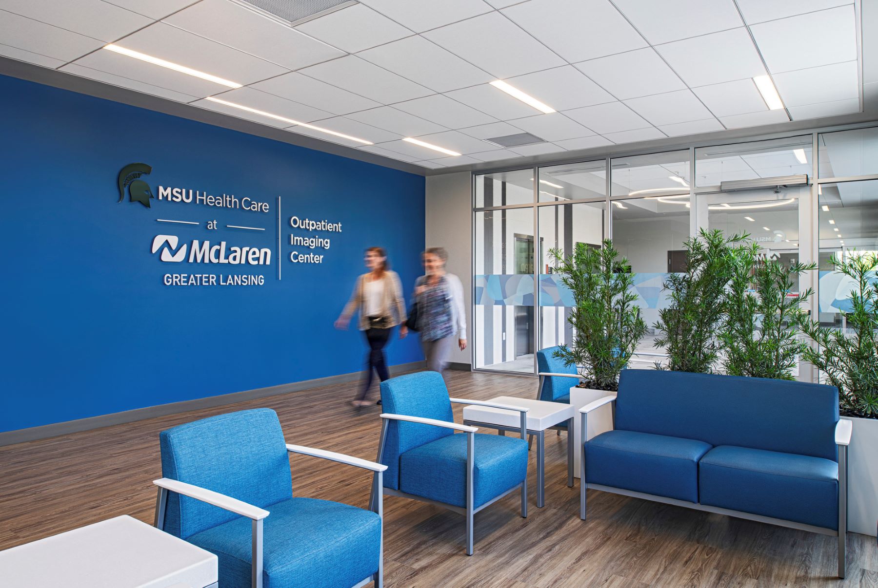 two people walking through an imaging center lobby with chairs, a couch and plants