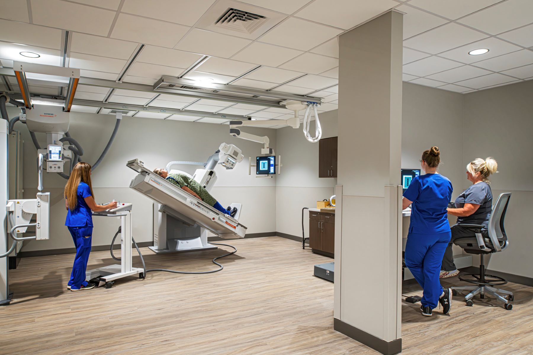 a nurse standing next to a an imaging machine and two radiologists looking at a computer screen