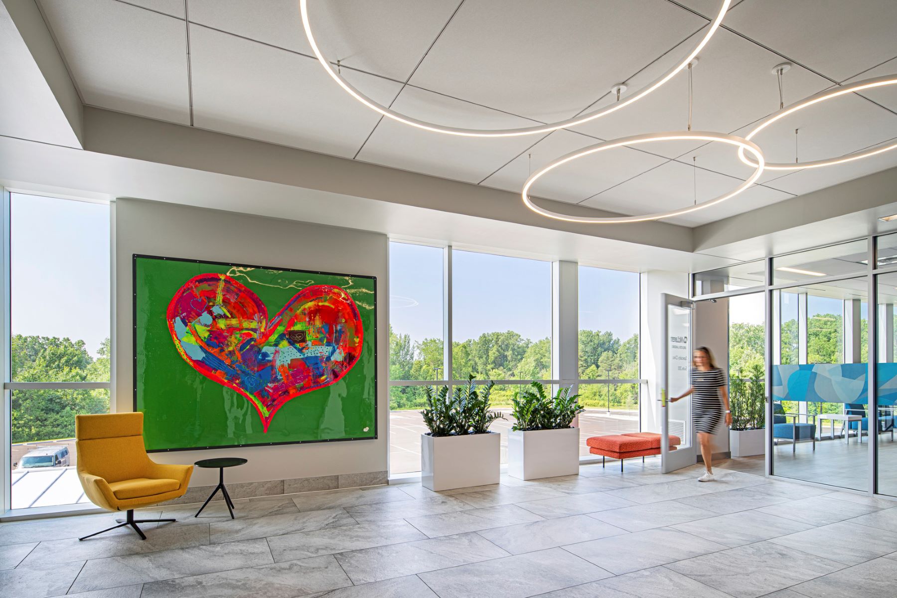 a person entering a lobby with a chair, table, plants and large artwork featuring an abstract heart