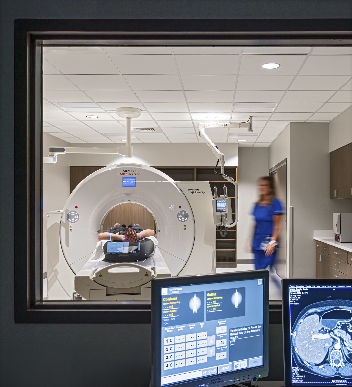 computer screens showing scans in a room looking into a room where a person is undergoing an imaging scan