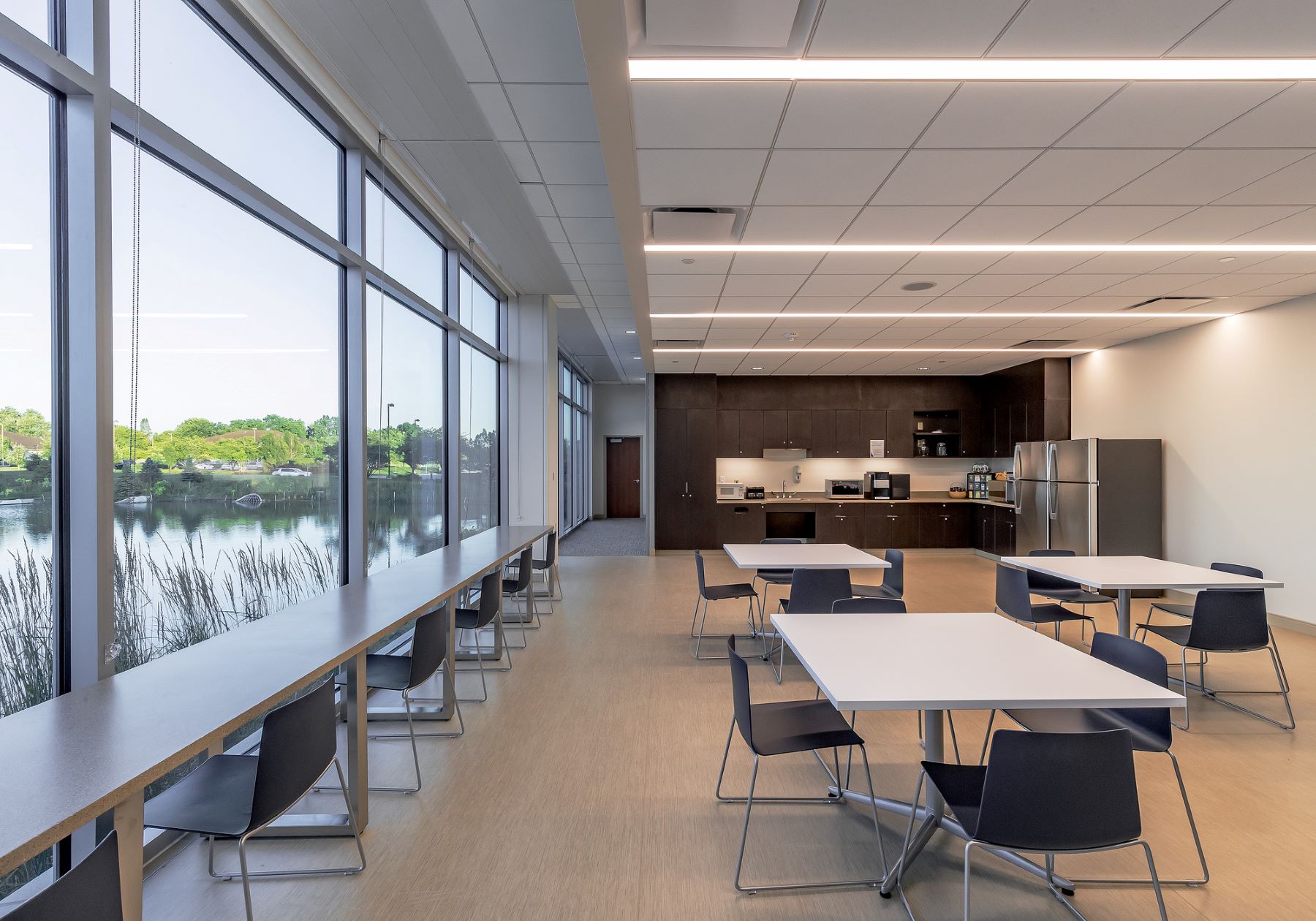 A staff break room with tables and chairs and large windows overlooking a pond