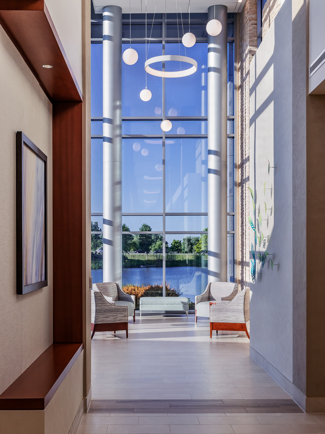 A corridor with two-story ceilings and large windows overlooking a pond