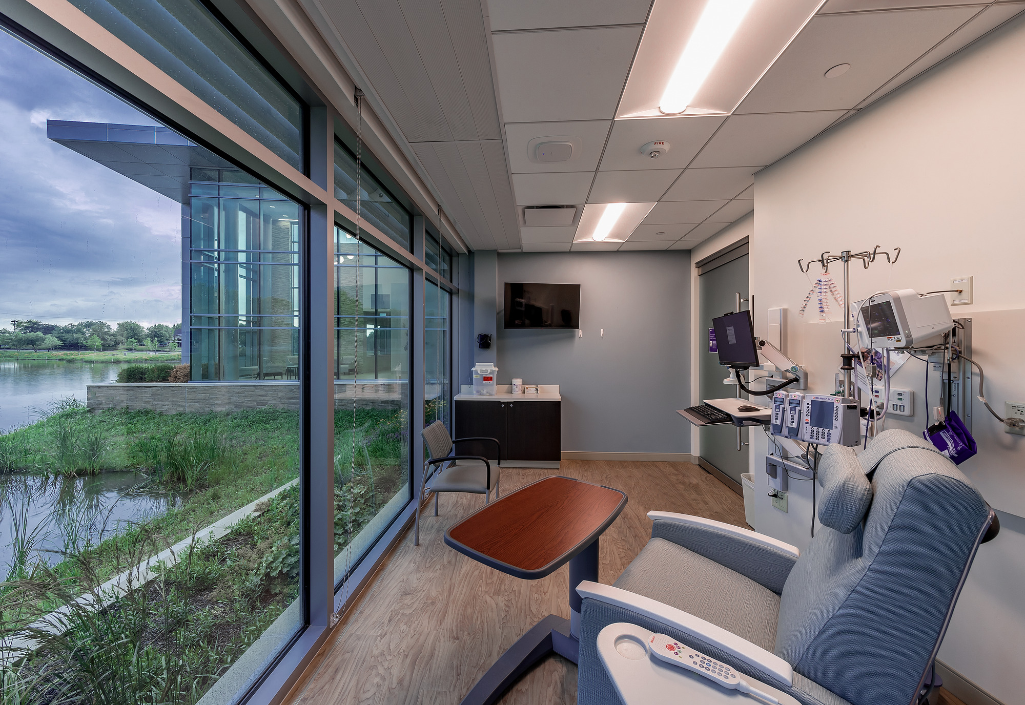 A cancer treatment infusion bay with floor to ceiling windows overlooking a pond