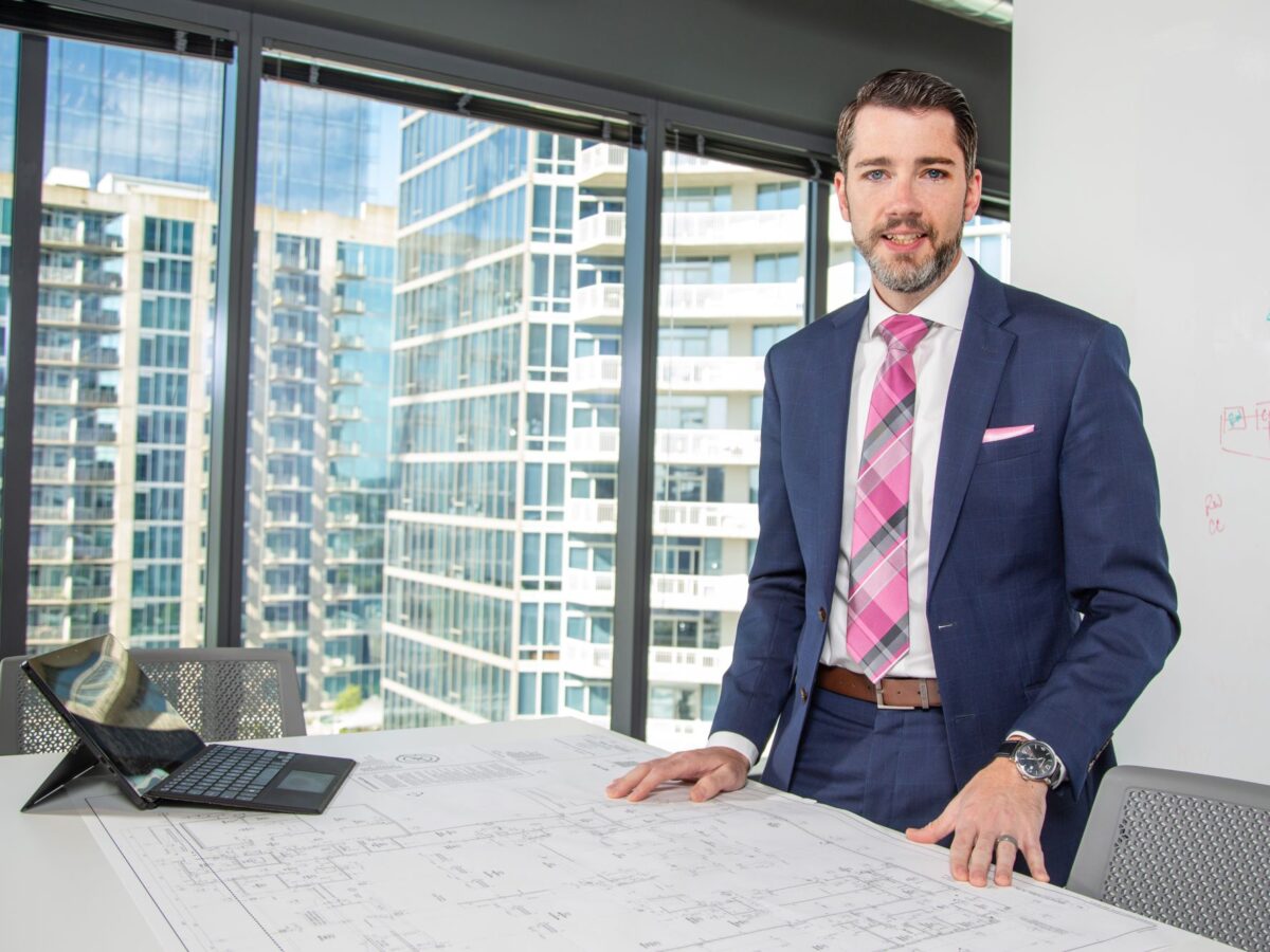 a man standing behind a table containing architectural plans and a laptop