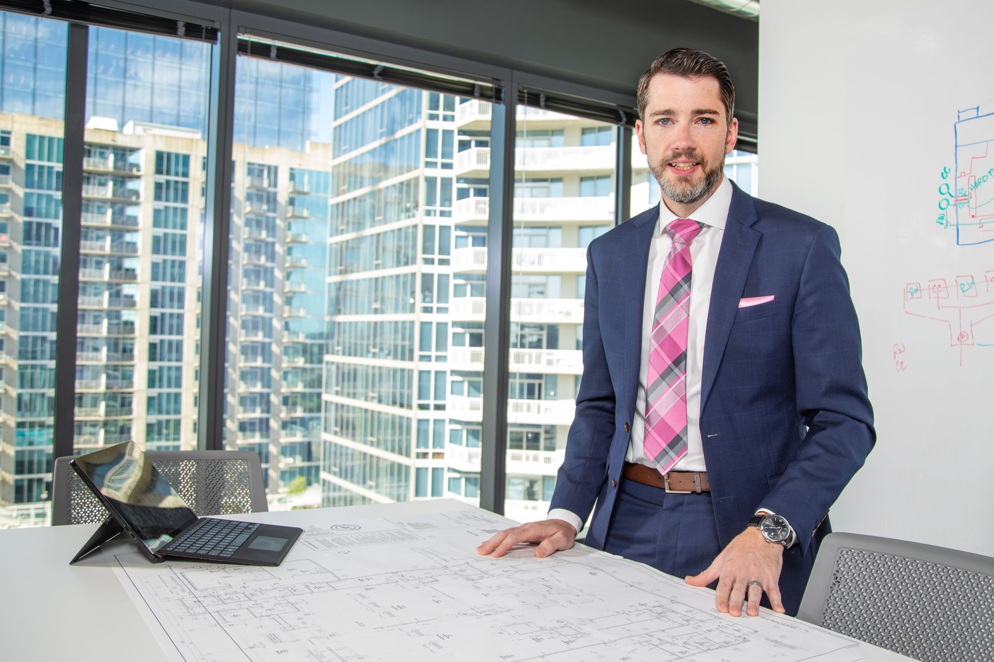 a man standing behind a table containing architectural plans and a laptop