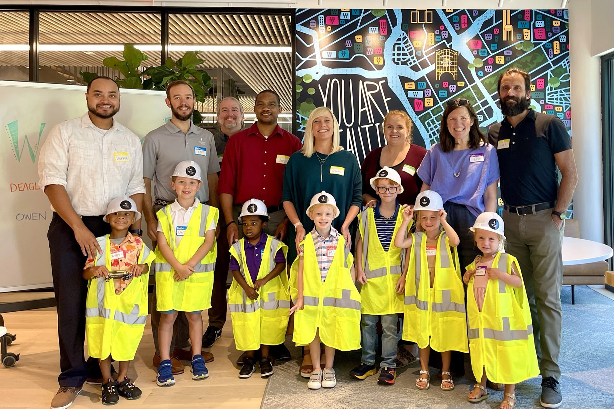 Children in safety vests and hard hats standing next to their parents in an office lobby