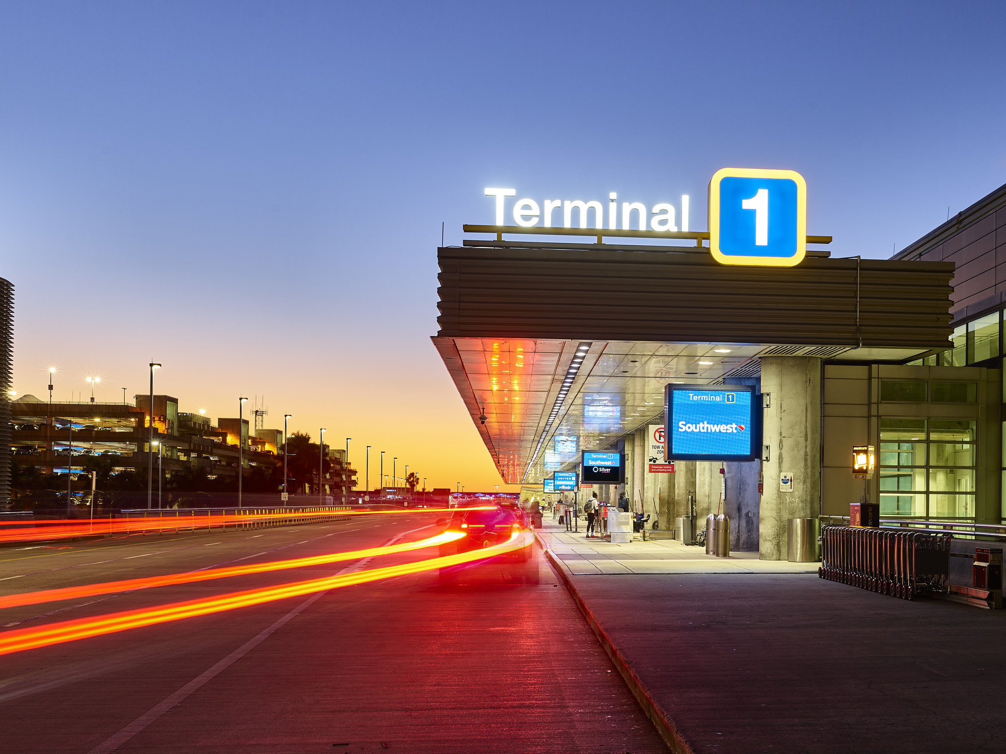 an airport terminal curbside at dusk with iluminated signs for airlines