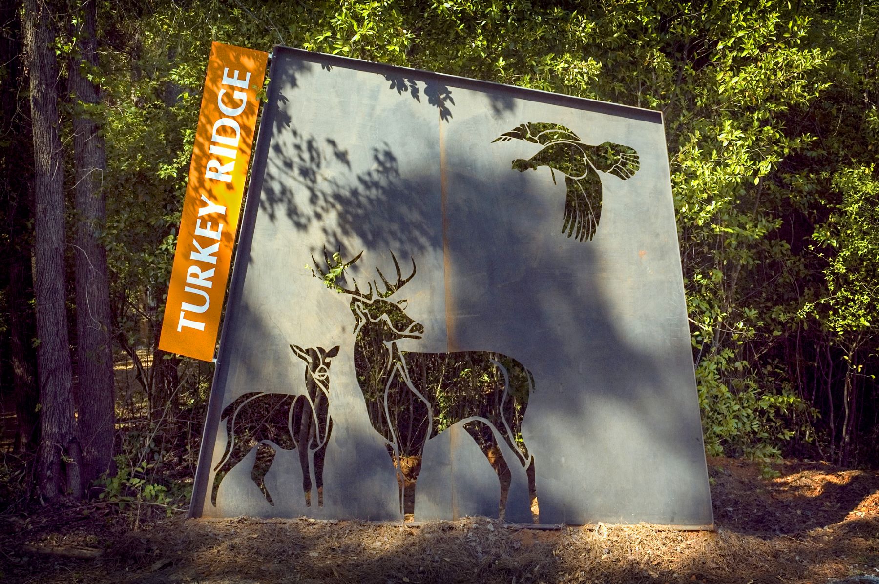 monumental directional sign made of a dark metal with cutouts of deer at a park