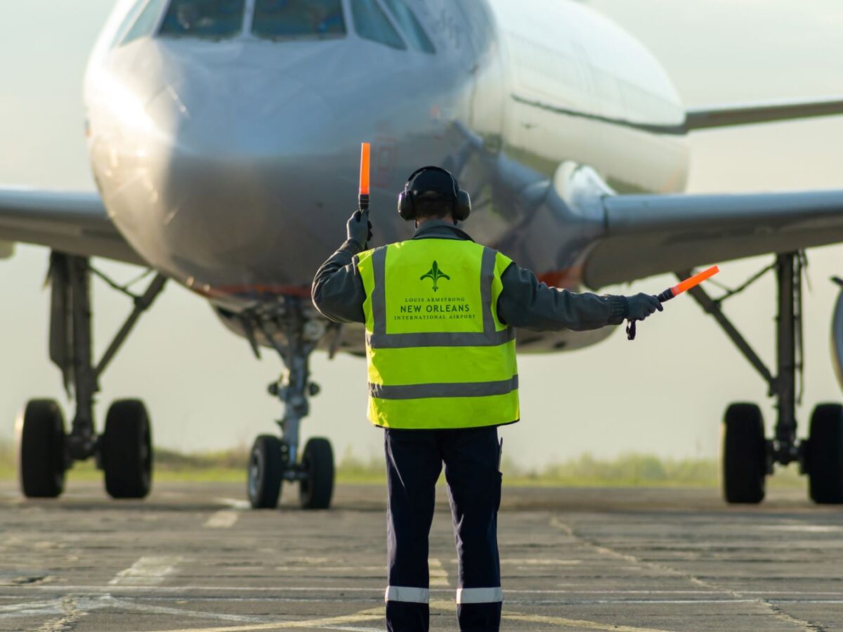 a person wearing a yellow safety vest directing an airplane on the runway at new orleans international airport