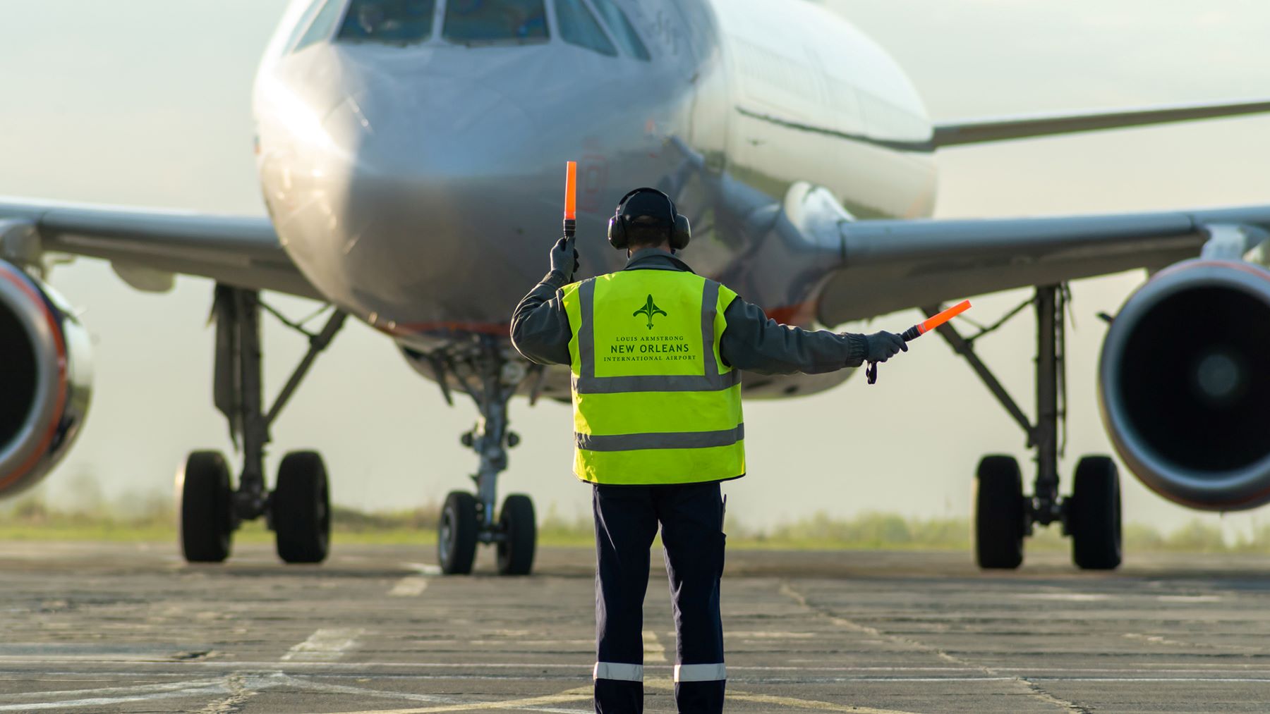 a person wearing a yellow safety vest directing an airplane on the runway at new orleans international airport